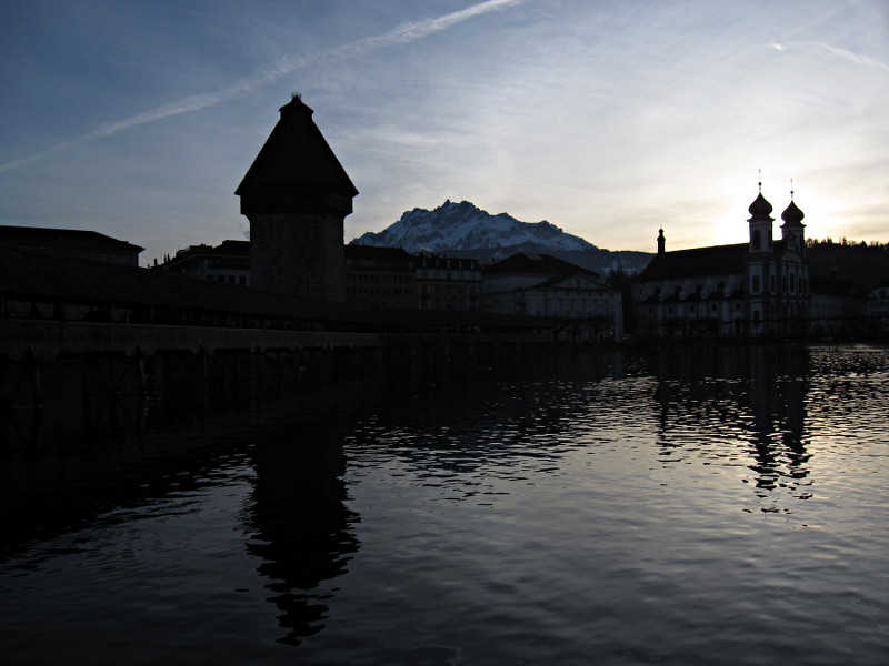 [Wasserturm e Jesuitenkirche si specchiano nelle acque del Reuss a Lucerna.  Sullo sfondo il Monte Pilatus.]